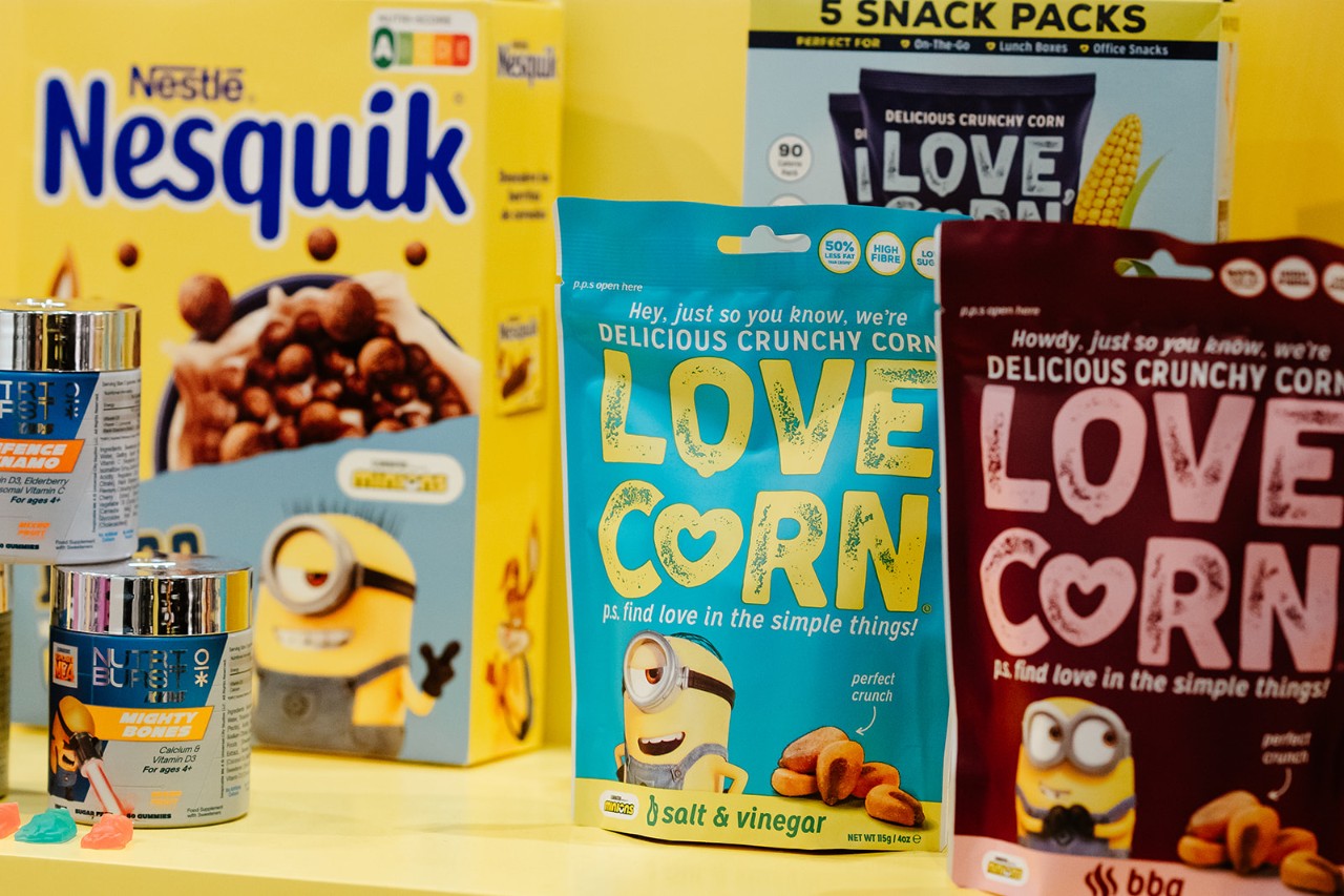 Minions-themed licensed food products including Nestlé Nesquik cereal, Love Corn crunchy snacks, and Nutriburst gummies displayed on a yellow background. Featuring brand collaborations with Minions characters for retail and grocery partnerships